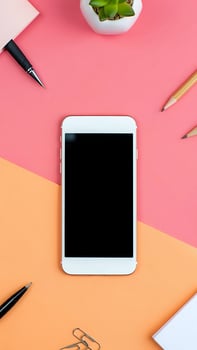Top view of modern smartphone mockup with blank screen on colorful workspace desk with office supplies and succulent plant photo