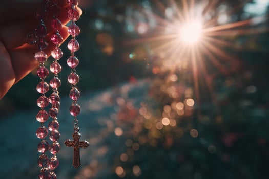 A rosary is held in the hand with the sun shining behind it photo