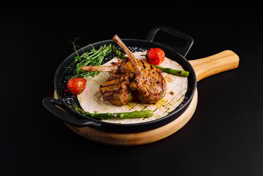 Grilled lamb chops served on a skillet with garnishes and fresh vegetables photo