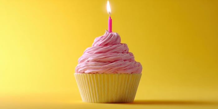 The cupcake with pink frosting and a lit candle on a vibrant background photo