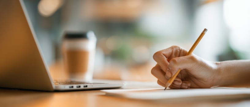 The focused hand writing notes next to a laptop and coffee cup. photo
