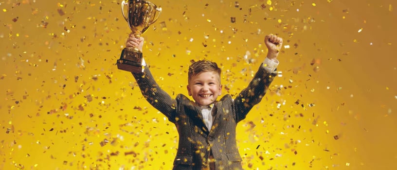 The joyful boy celebrating victory with a trophy and confetti falling around. photo