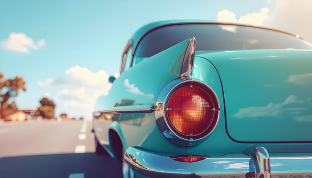 A close-up detail of the rear corner section of a vintage automobile, featuring teal green paint, a chrome bumper, and a visible taillight. photo