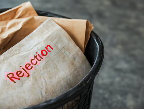 Rejection paper in trash bin with crumpled brown paper inside, symbolizing failure and discarded plans in blurred background photo