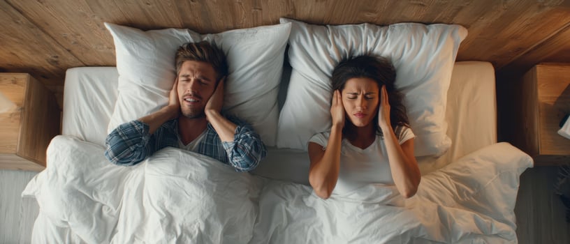 The couple showing frustration while trying to sleep amidst noise disturbances. photo