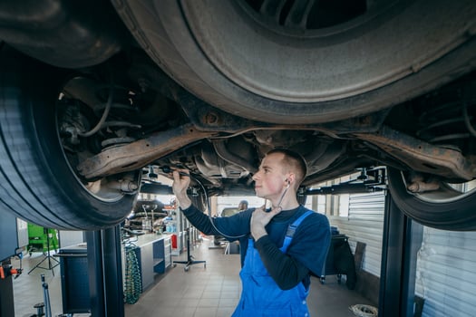 Young car mechanic at repair service station inspecting car wheel and suspension detail of lifted automobile. photo