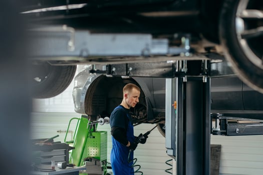 Young car mechanic at repair service station inspecting car wheel and suspension detail of automobile photo