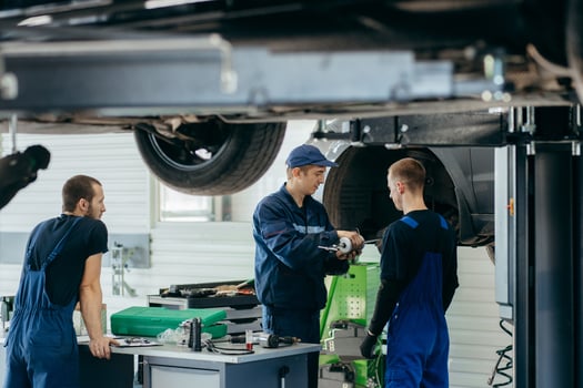 Young car mechanics at repair service station inspecting car wheel and suspension detail of lifted automobile photo