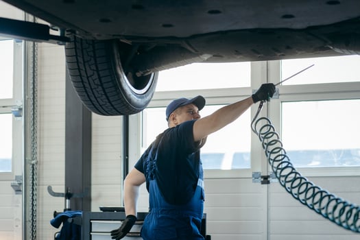 Adult car mechanic at repair service station inspecting car wheel and suspension detail of lifted automobile. photo
