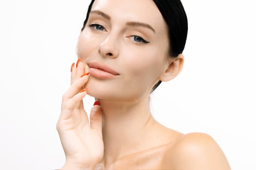 Beautiful woman with clear skin gently touching her face, showcasing flawless complexion and vibrant nails, against a clean white background, emphasizing beauty and self-care concepts photo