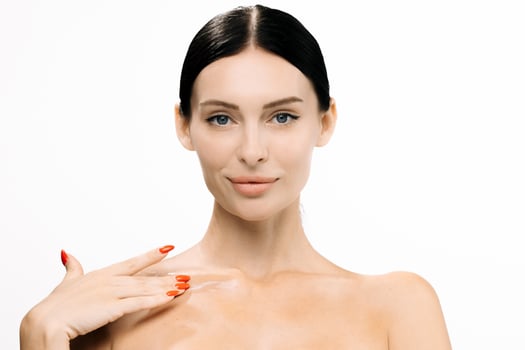 Beautiful woman with clear skin applying skincare product on shoulder, showcasing beauty routine against a white background, emphasizing healthy skin and self-care practices photo