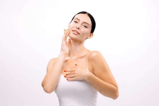 Young woman with clear skin gently touching her face, showcasing a natural beauty routine against a bright white background, emphasizing skincare and self-care practices photo