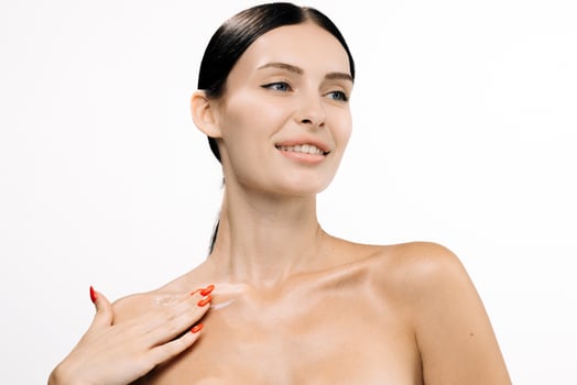 Woman applying rejuvenating serum on her shoulder, showcasing radiant skin and healthy glow, with a soft focus background emphasizing beauty and skincare routine photo