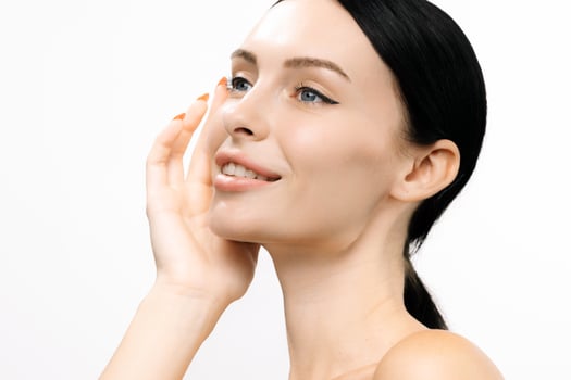 Young woman with clear skin gently touching her face, showcasing a natural beauty routine against a clean white background, emphasizing skincare and self-care practices for healthy skin photo