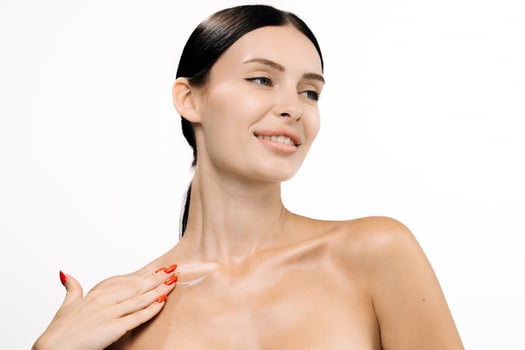 Beautiful woman with clear skin applying moisturizer on her shoulder, showcasing a radiant complexion against a clean white background, emphasizing skincare and beauty routine photo