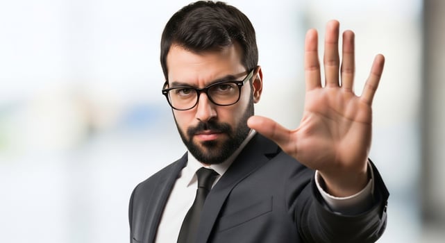 Serious businessman in suit and glasses holds hand up, signaling stop photo