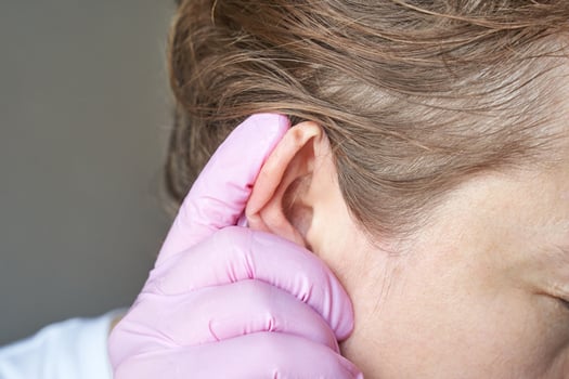 close up of female adult with caucasian skin having ear examined by doctor wearing pink gloves. photo