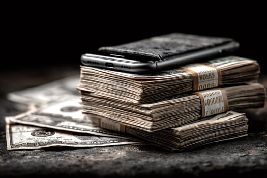 Smartphone and wallet resting on stacks of dollar bills photo