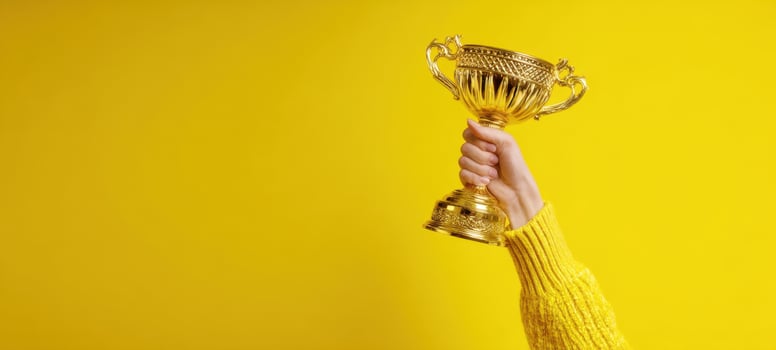 The hand proudly holding a golden trophy against a bright yellow background photo