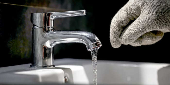 Plumbers Gloved Hand Fixing Faucet In Contemporary Bathroom photo