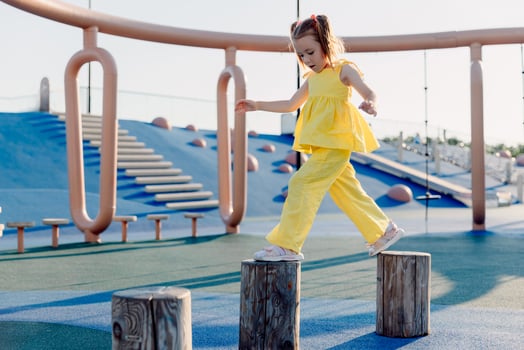 Little girl in yellow dress balancing on playground stumps, focused and active on a sunny day. photo