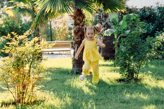 Energetic little girl in yellow dress running joyfully through green garden on a sunny summer day. photo