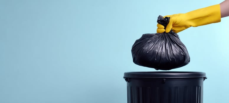 The hand dropping a black garbage bag into a trash can. photo