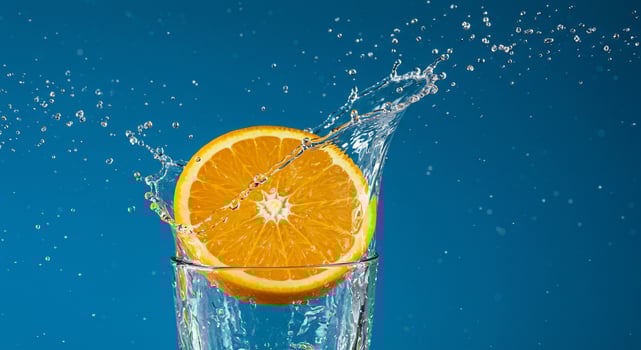 Fresh orange slice splashing into a glass of clear water against a blue background. photo