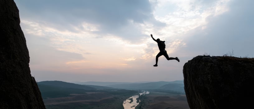 The adventurous person jumping between cliffs at sunset over a scenic river photo