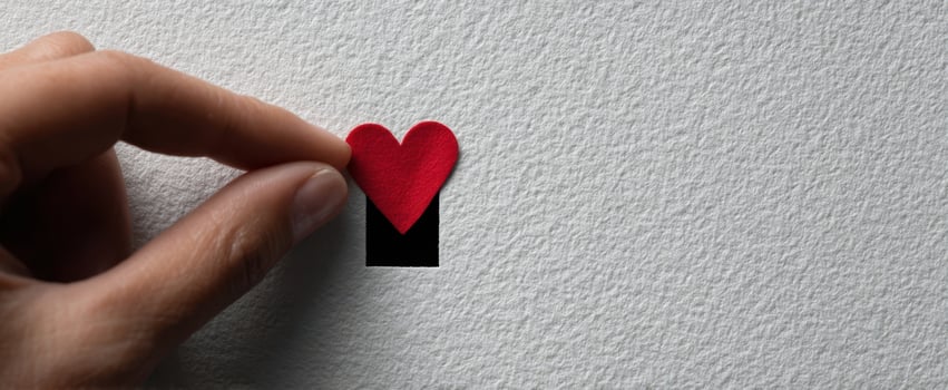 The hand positioning a red heart on a textured black background. photo