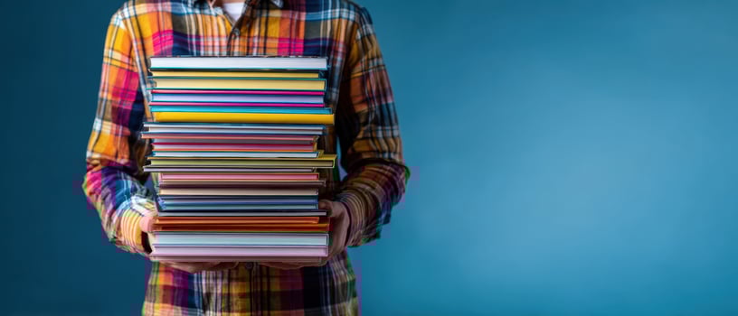 The colorful stack of books held by a person in a plaid shirt. photo