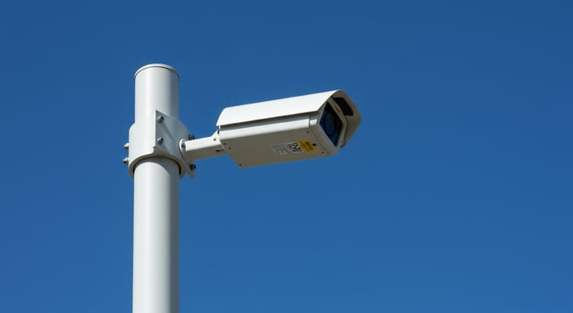 Security Camera Against a Vibrant Blue Sky on a White Pole photo