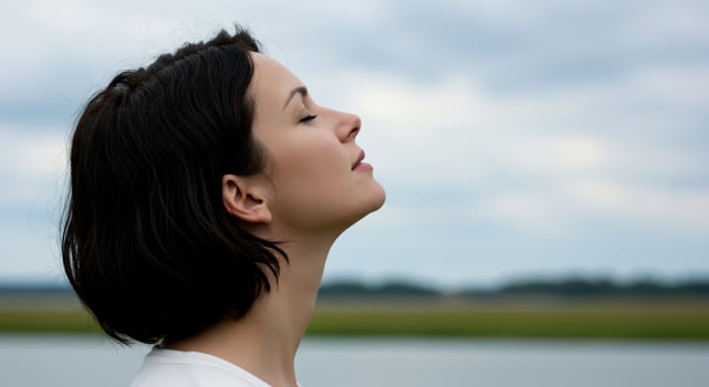 Serene Woman Inhaling Fresh Air by a Tranquil Lake Under Cloudy Sky photo
