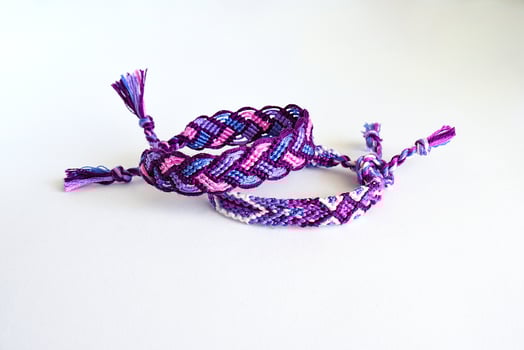 Multicolored purple woven DIY friendship bracelets handmade of embroidery bright thread with knots isolated on white background photo