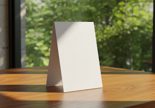 Blank white tent card on wood table in front of green foliage for messages photo