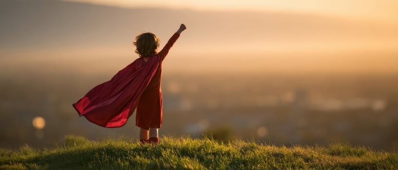 The child in a red cape stands triumphantly against the sunset sky. photo