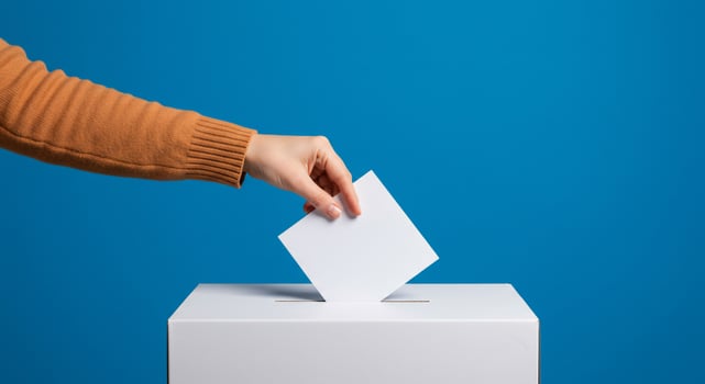 Hand Casting a Vote in a Ballot Box on Blue Background photo
