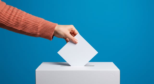 Hand Casting a Vote in a Ballot Box on Blue photo