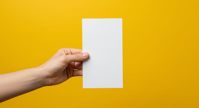 Hand holding blank flyer against vibrant yellow background. photo