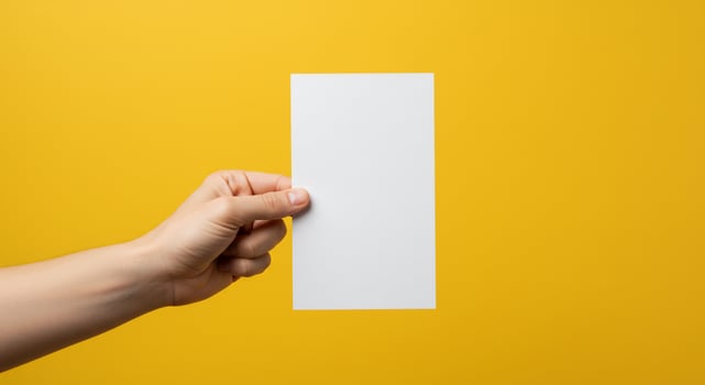 Hand holding blank sheet of paper on yellow background photo