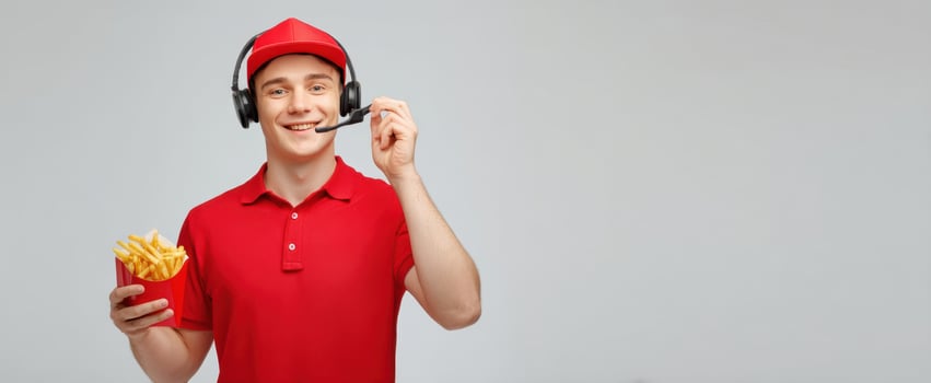 The cheerful delivery worker holding fries while using a headset. photo