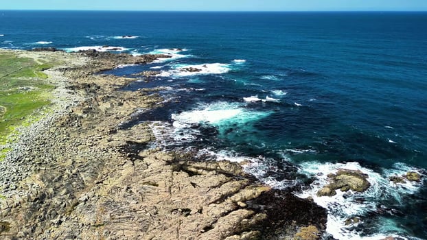 Experience breathtaking aerial views of a stunning rocky coastline and vibrant blue ocean waves photo