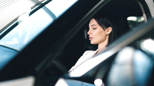 Woman sitting in car showroom, thoughtfully considering vehicle options, surrounded by modern cars and bright showroom lighting, showcasing car buying experience photo
