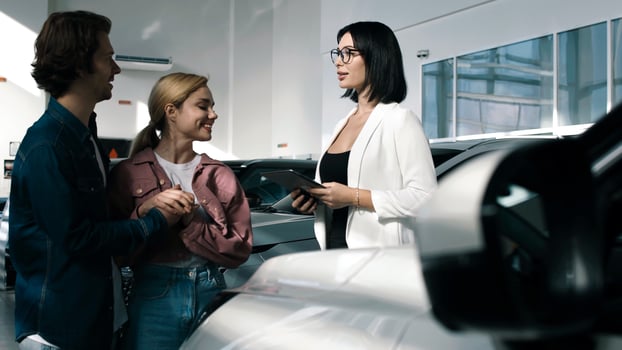 Couple engaging with a car dealer in a modern showroom, discussing vehicle options while surrounded by various cars and bright lighting photo