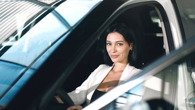 Confident woman in a car showroom, sitting inside a vehicle, showcasing the modern interior and bright ambiance of the dealership environment photo
