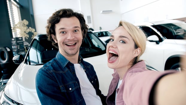 Happy couple taking a selfie in a modern car showroom, surrounded by sleek vehicles, capturing the excitement of buying a new car photo