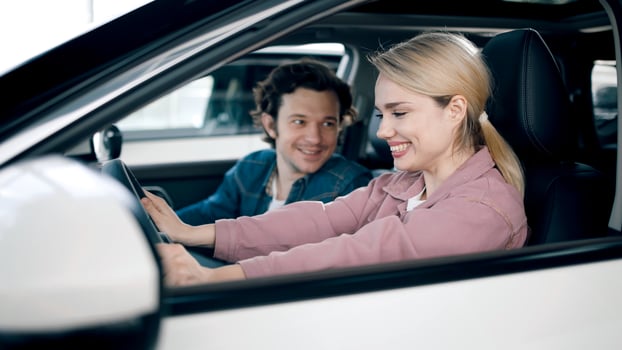 Young woman is joyfully testing car features while man observes in a modern car showroom, showcasing excitement of buying a new vehicle photo