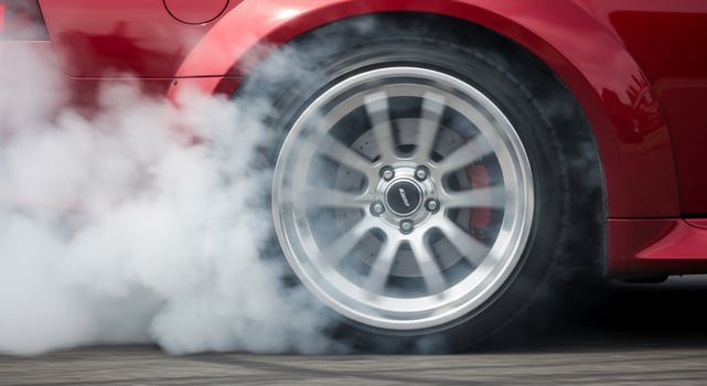 A red sports car is driving on the road with smoke coming out of the wheels photo