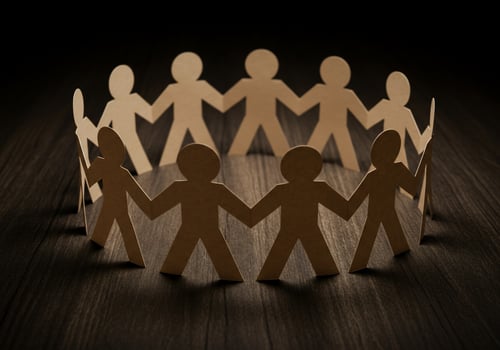Team of paper doll figures holding hands in circle on dark wood background photo