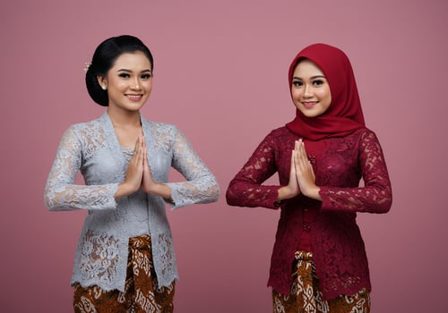 Two smiling women in kebaya greet, background is pink, use celebration, event photo